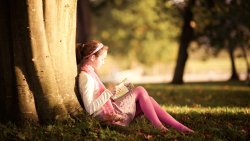Little Girl Reading Book Under a Tree in the Park